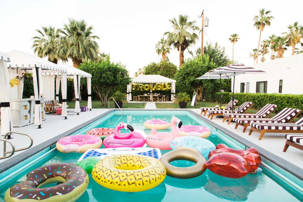 A backyard pool with flaming, donut sprinkles, and red gummy bear floats. 