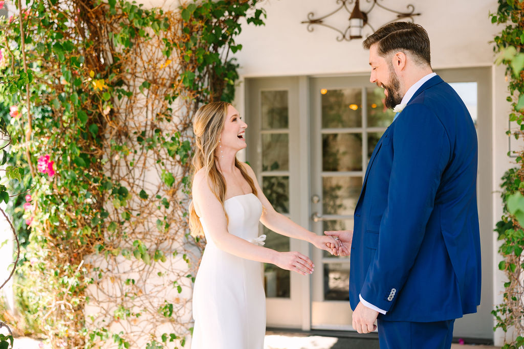 A bride laughs during her first look with her groom in a blue suit