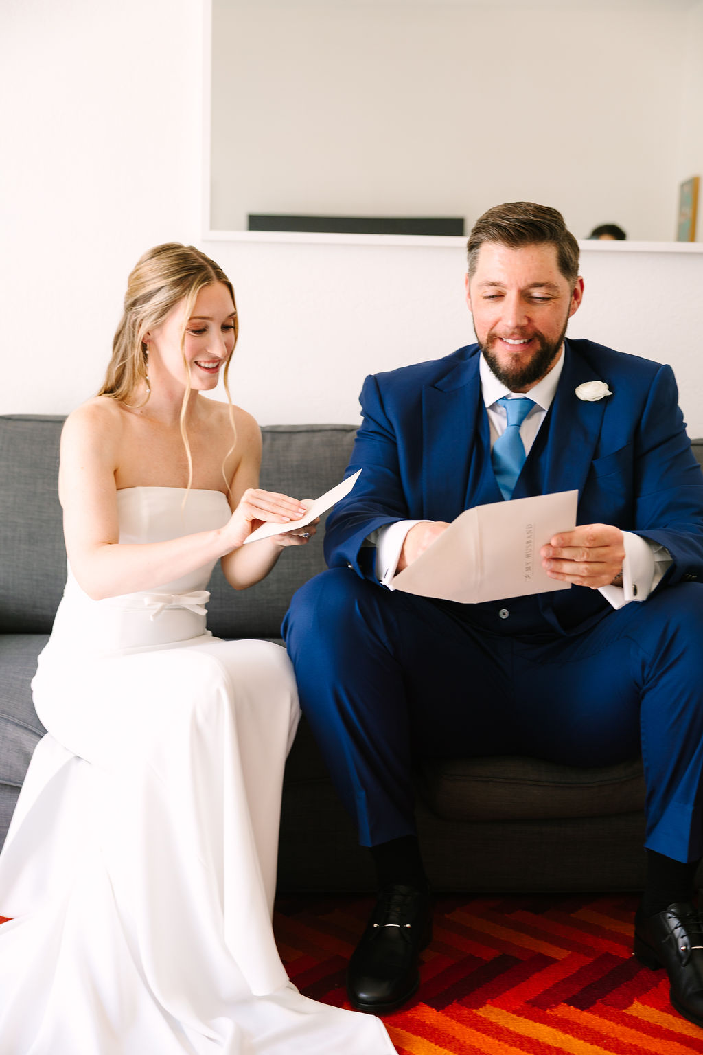 A bride and groom sit on a couch reading notes to each other before their ceremony