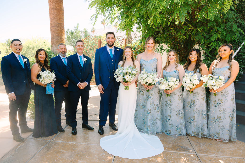 Newlyweds smile while standing with their wedding party on a patio