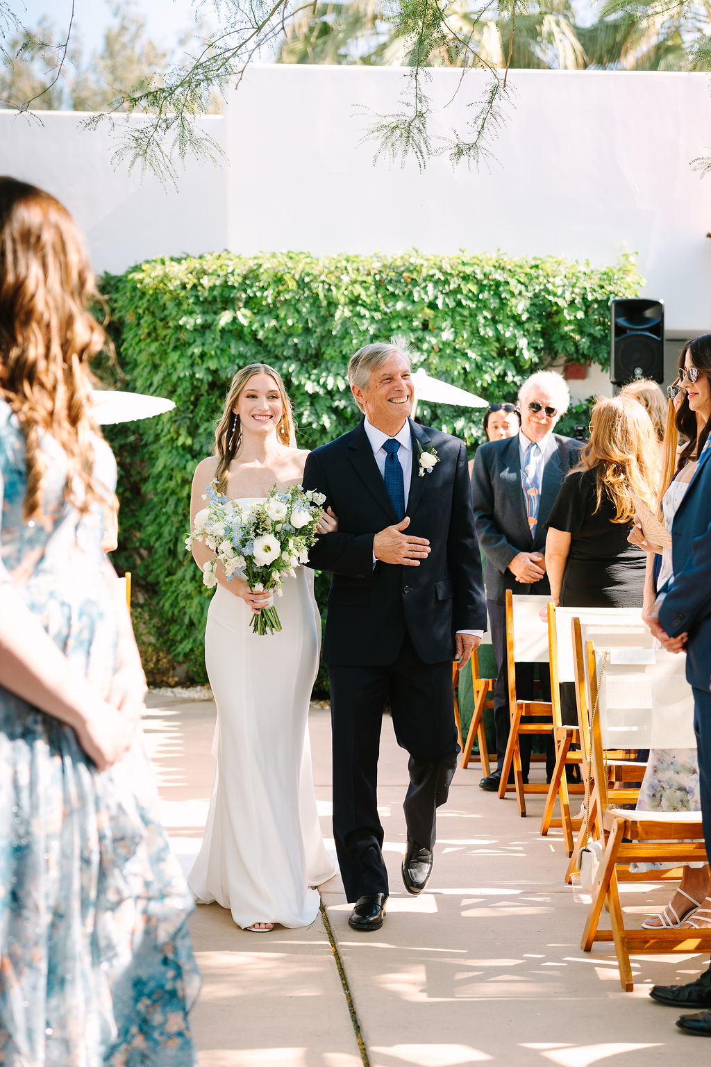 A happy father smiles while walking his daughter down the aisle to her alcazar palm springs wedding ceremony in a garden