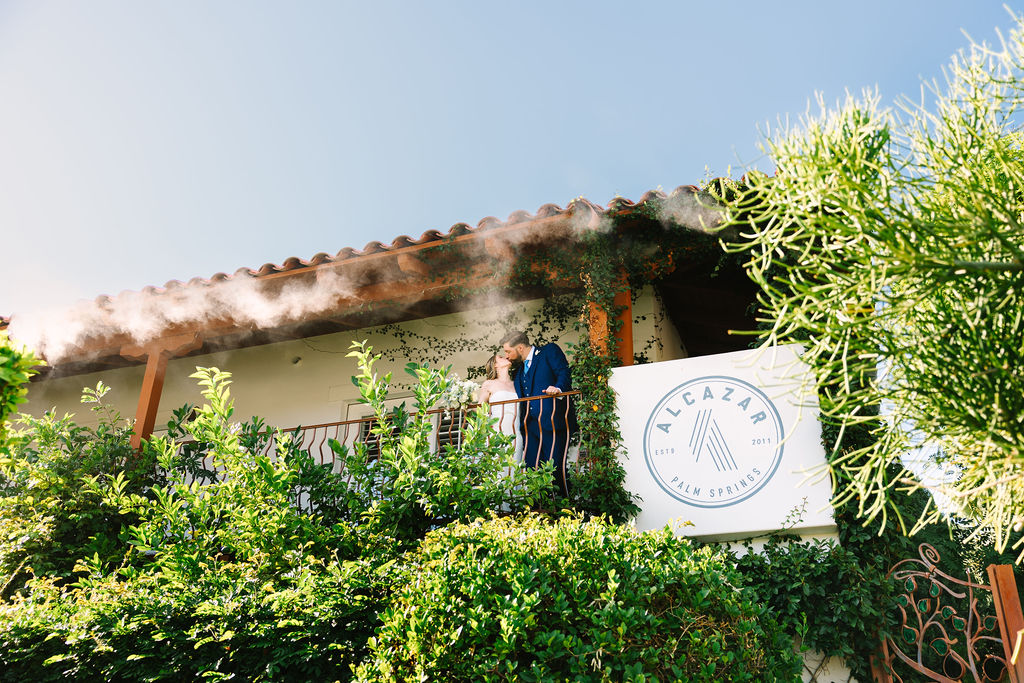 Newlyweds kiss on the balcony by the alcazar palm springs wedding venue sign