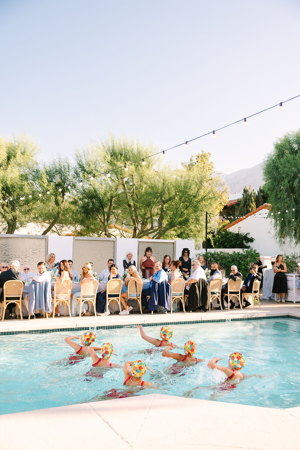 Synchronized swimmers put on a show in colorful swim caps as guests watch at an alcazar palm springs wedding