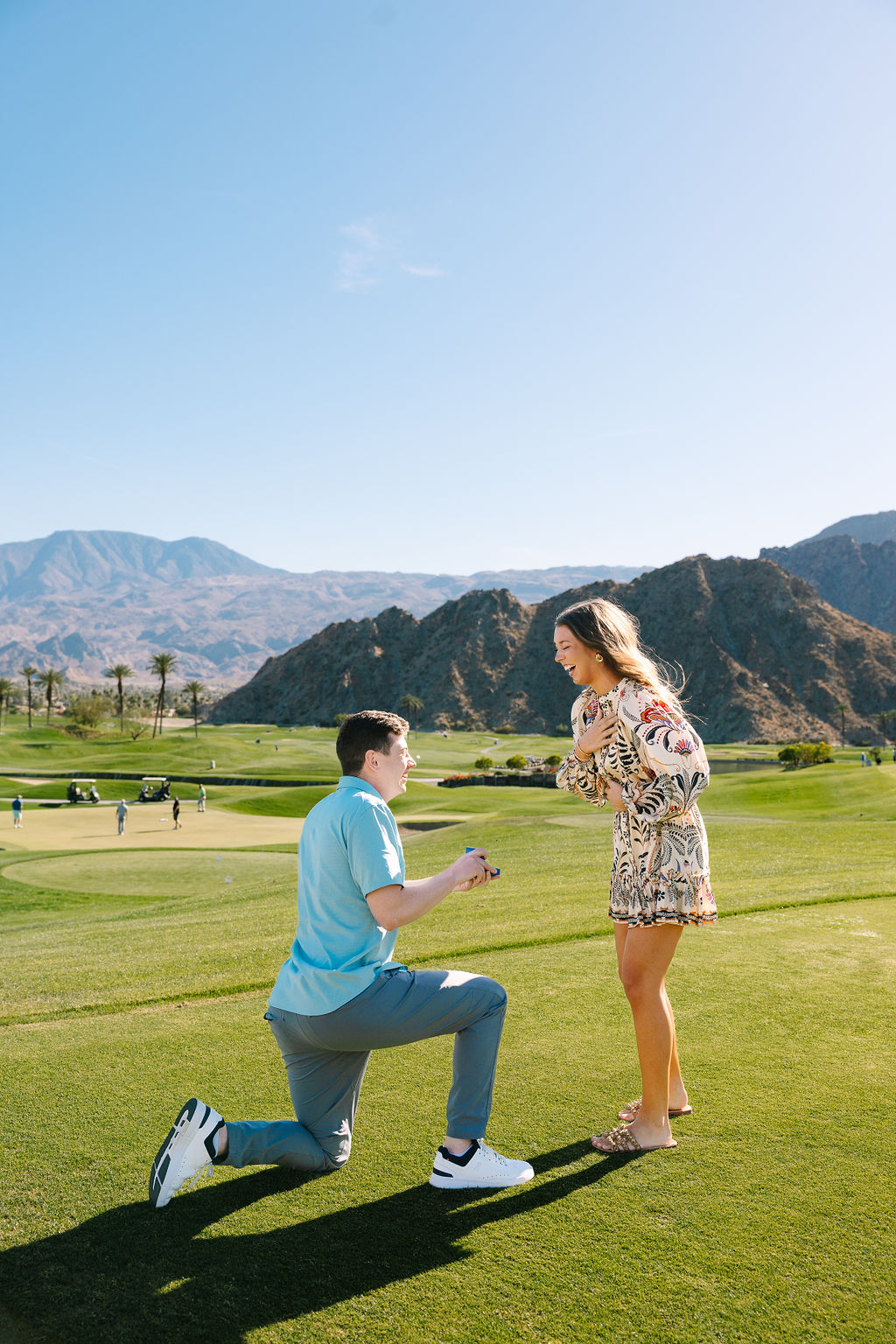 A woman holds her heart as she is proposed to on one knee on a golf green