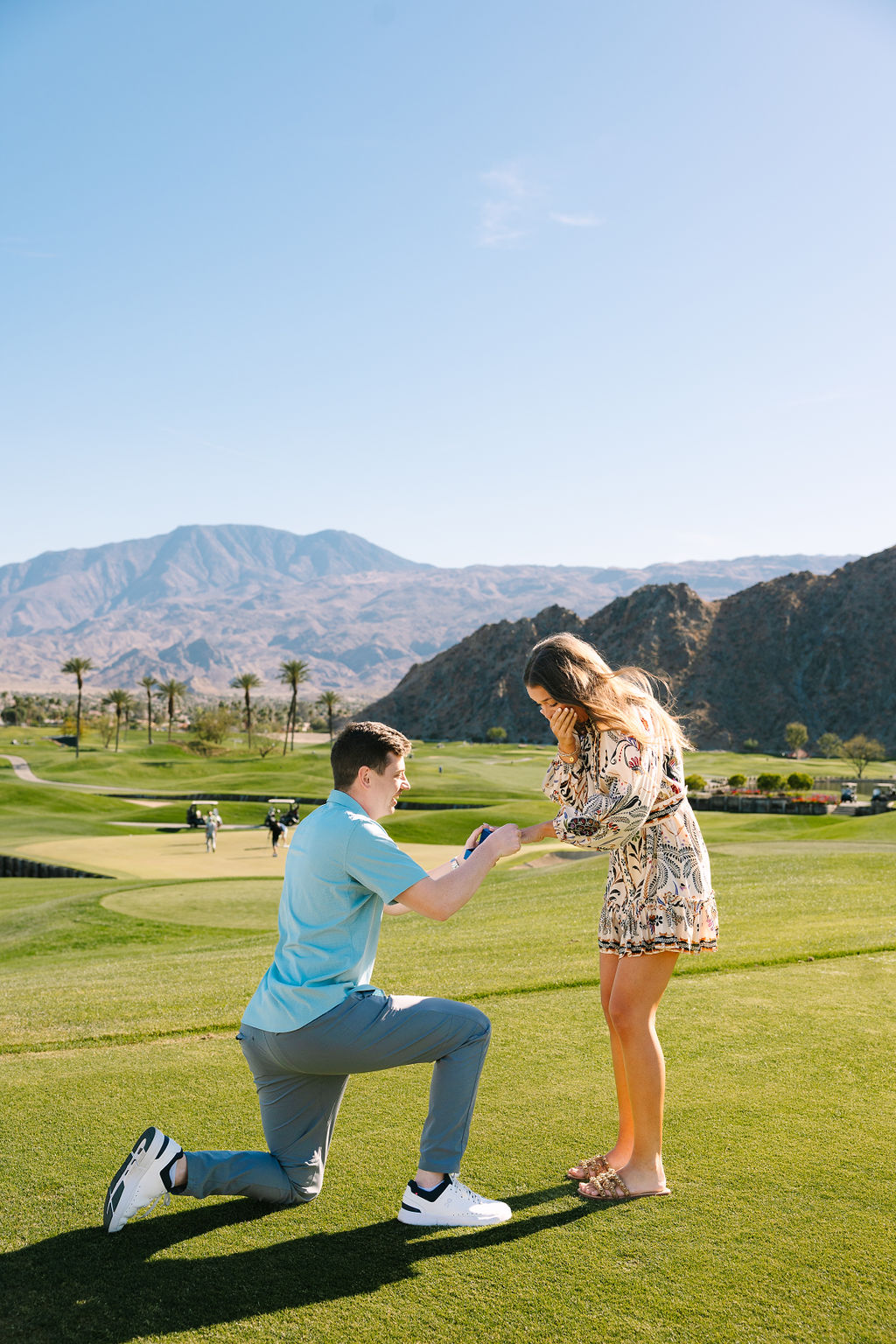 A man on one knee proposes and puts the ring on his new fiancee on a pga west pete dye mountain course putting green