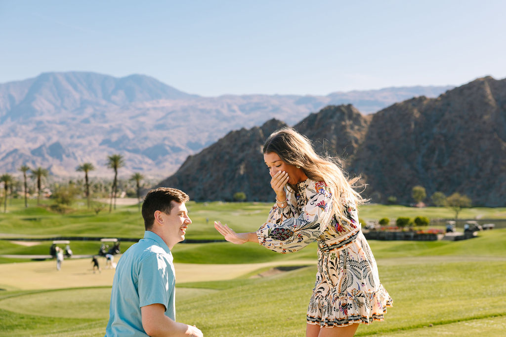 A woman in shock admires her new engagement ring during her proposal with the man still kneeling