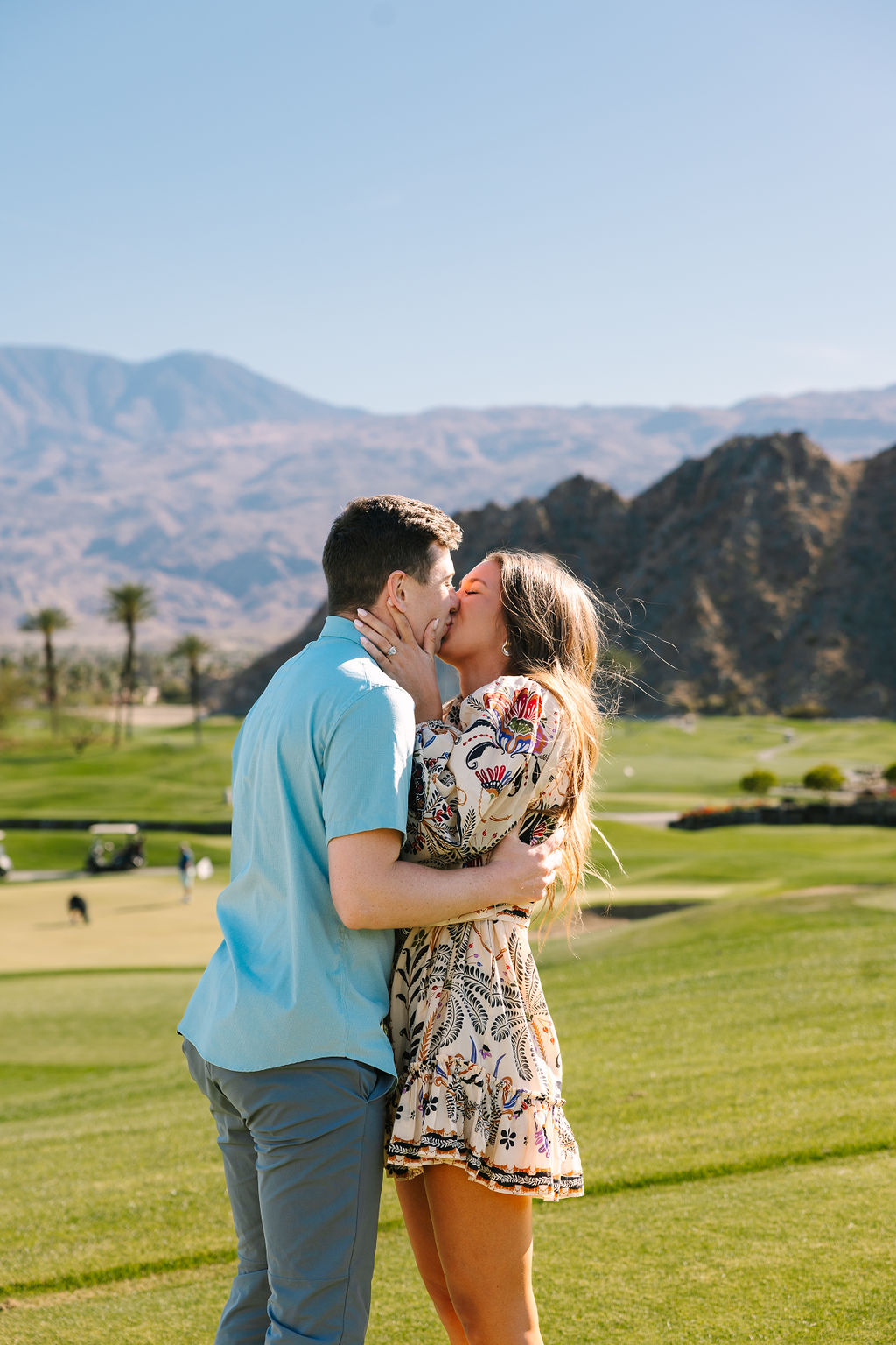 An engaged couple kiss passionately after the proposal in a blue shirt and floral print dress