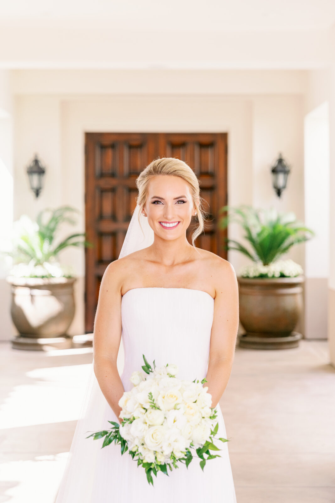 A smiling bride holding her white bouquet in a patio at the la quinta country club wedding venue