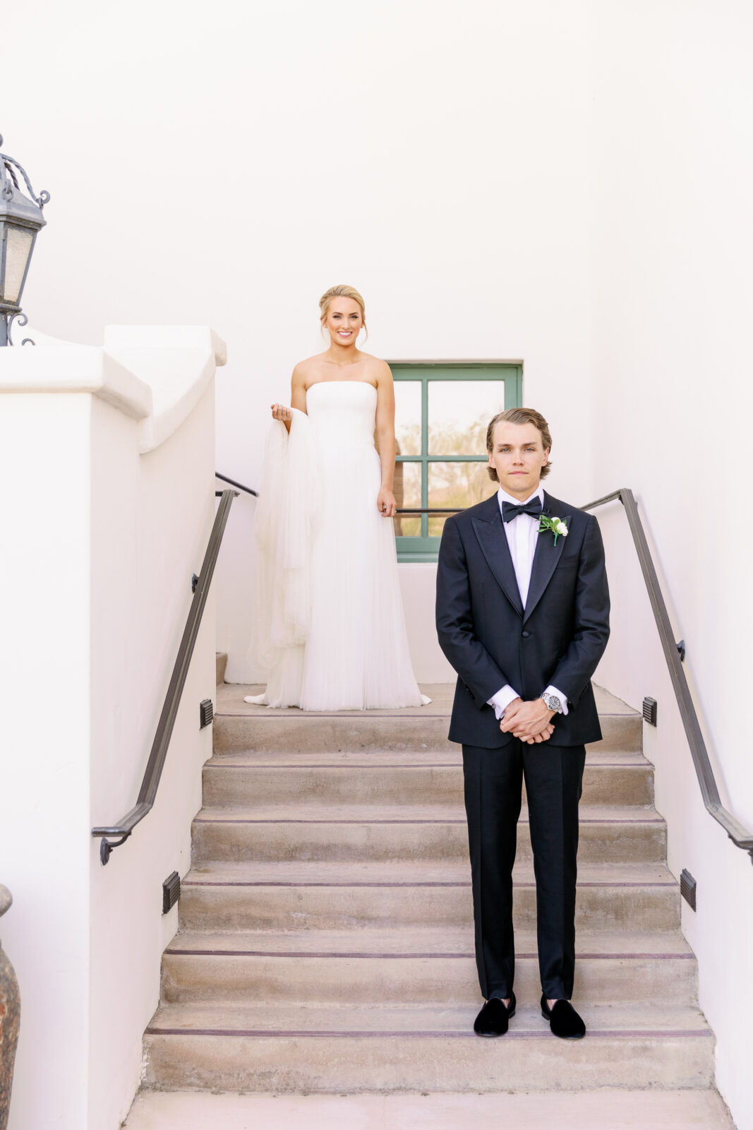 A groom nervously awaits his bride on the stairs behind him for their first look