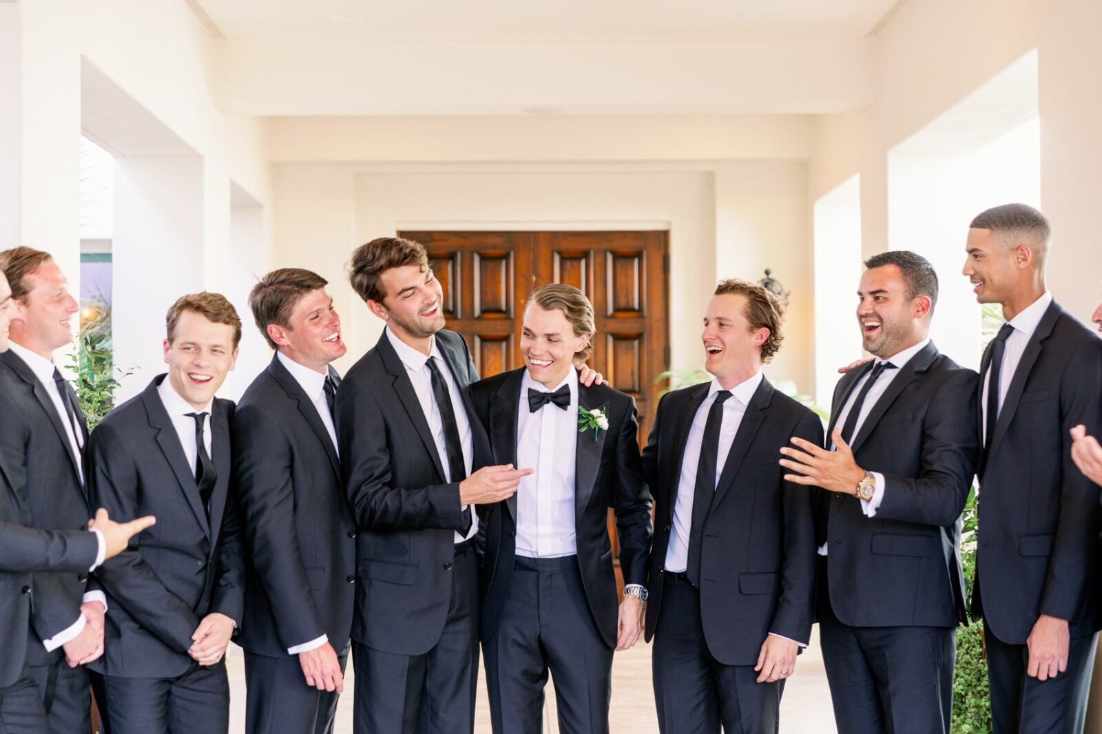 A groom laughs with her groomsmen in black suits