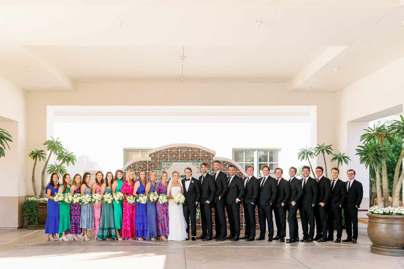 A bride and groom stand with their large wedding party in the lobby by a fountain