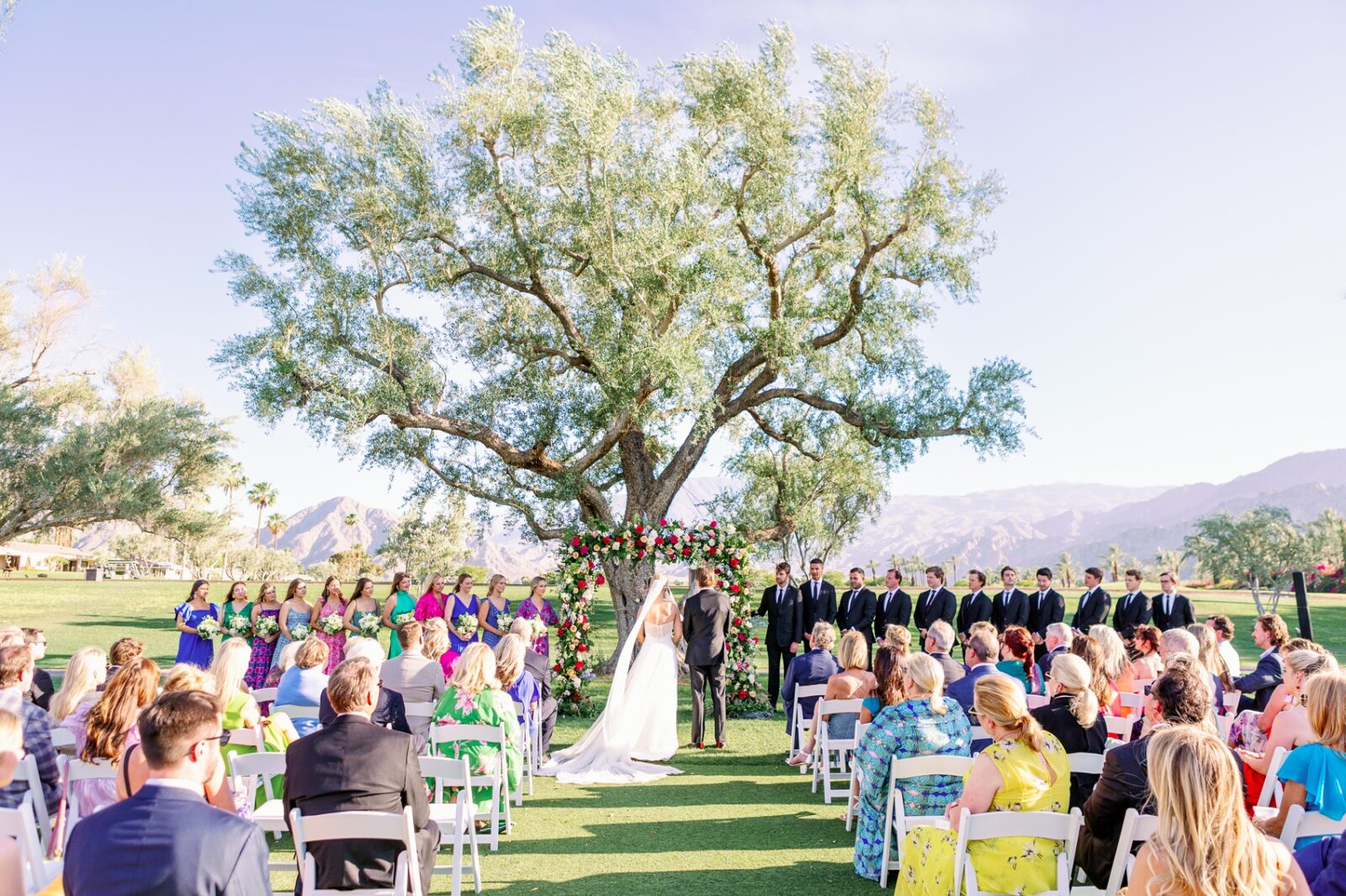 A bride and groom stand under the tree at the altar during their la quinta country club wedding ceremony under a large tree