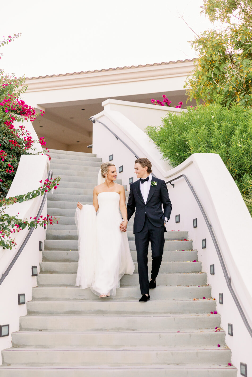 A groom helps his bride down the stairs as they smile at each other at their la quinta country club wedding