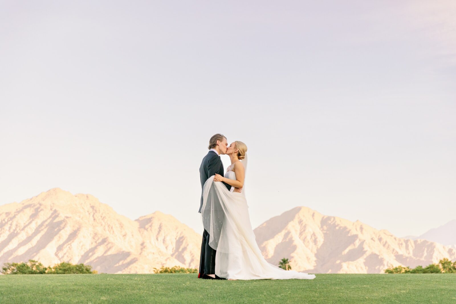 A bride and groom kiss at sunset on a golf green at their la quinta country club wedding