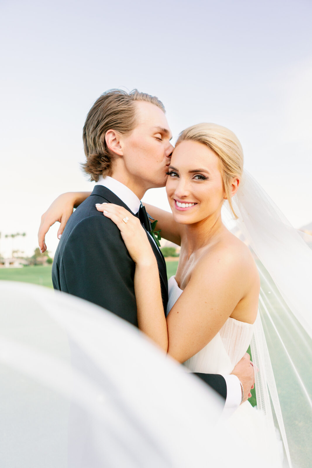 NEwlyweds snuggle and kiss the smiling bride on a golf course