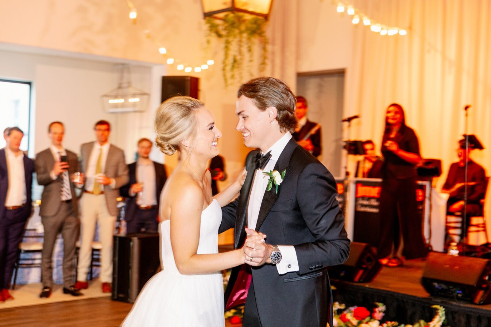 A bride and groom laugh and dance to a live band as guests watch