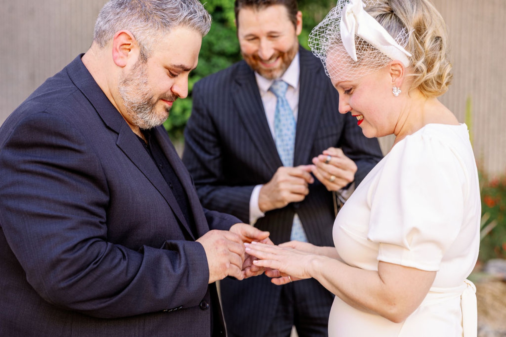 A groom in a black suit puts the ring on his bride as the officiant smiles behind them at their palm springs art museum wedding ceremony