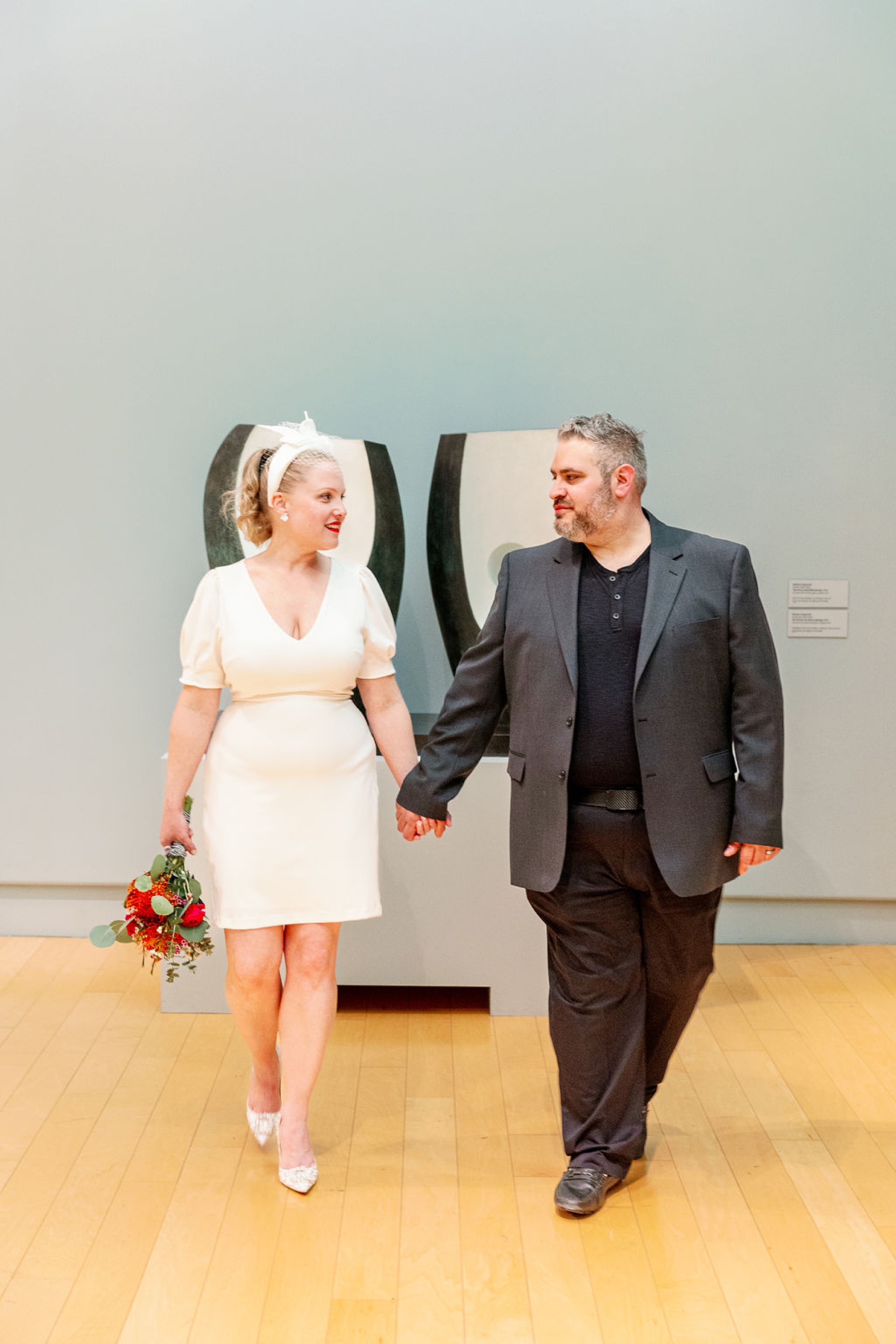 A happy couple smiles at each other while holding hands and exploring a museum