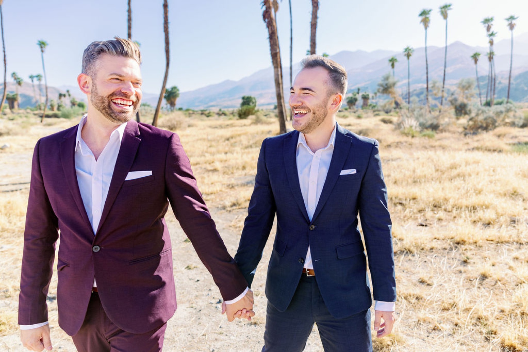 A big laugh shared by an engaged couple in blue and purple suits as they walk in a trail captured by a palm springs engagement photographer
