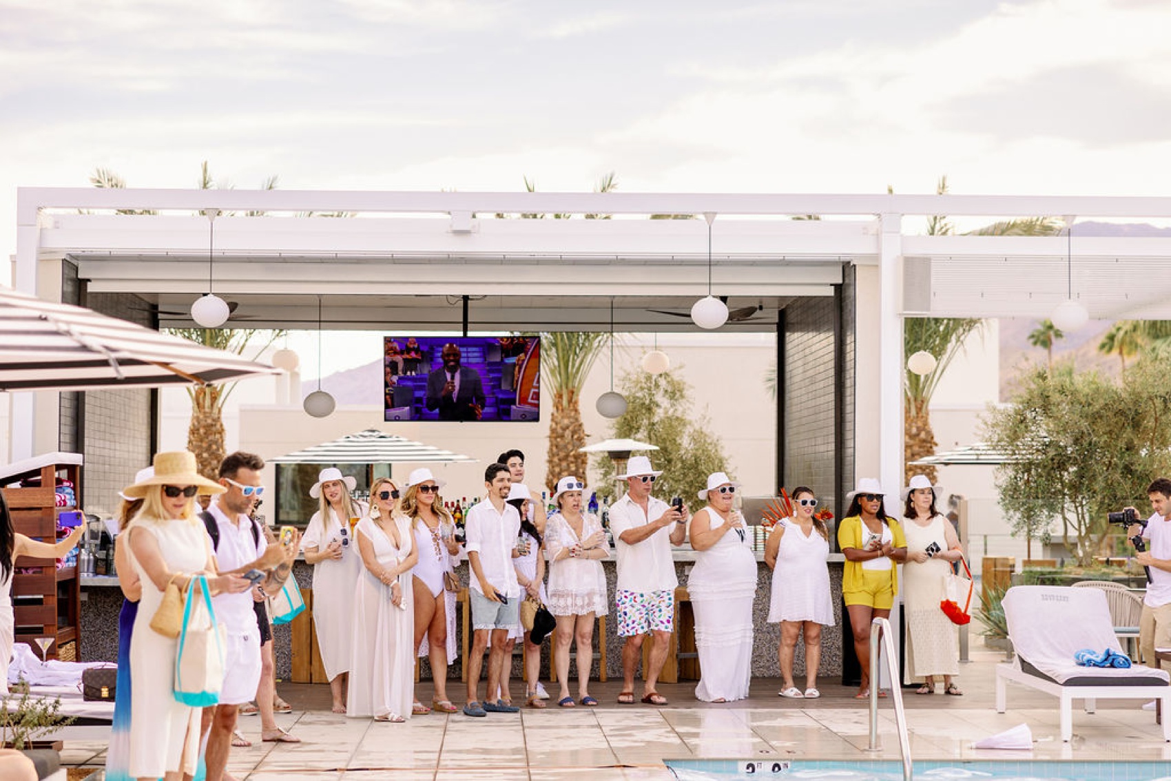 A large group stands by the bar taking photos and watching a performace with everyone in white