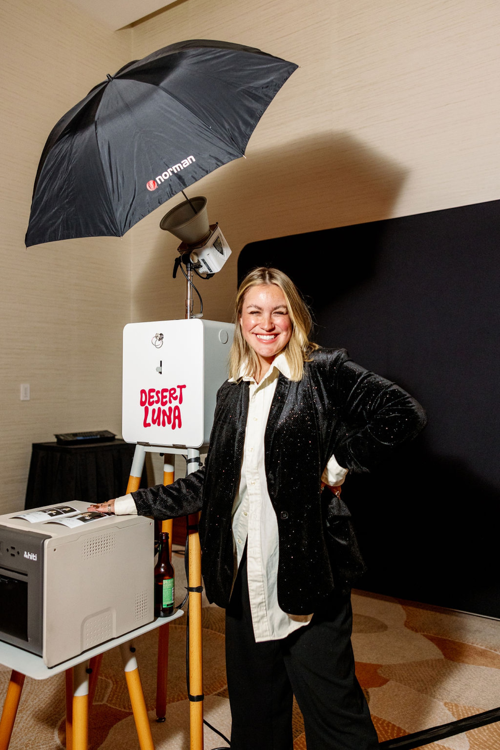 A happy woman in a black jacket smiles next to a photo booth with printer