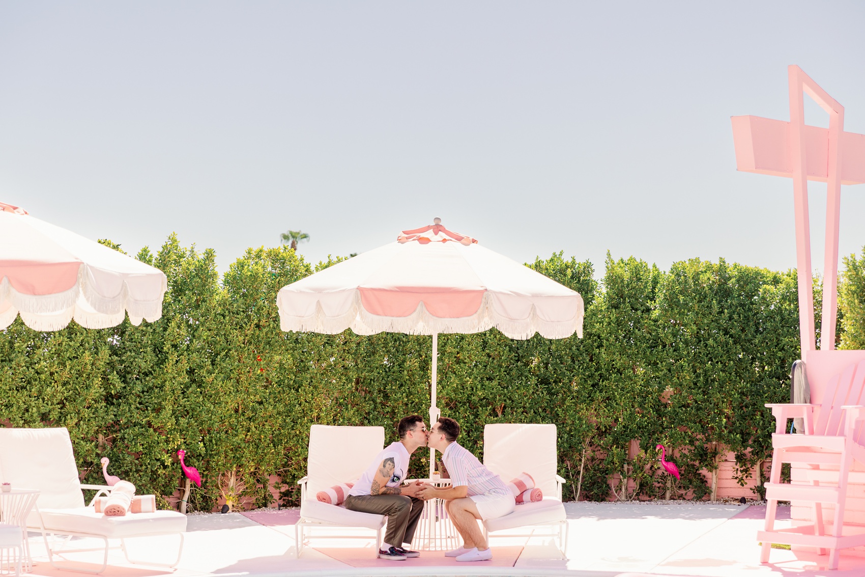 A happy couple kisses under a pool umbrella while sitting on poolside beds at trixie motel palm springs