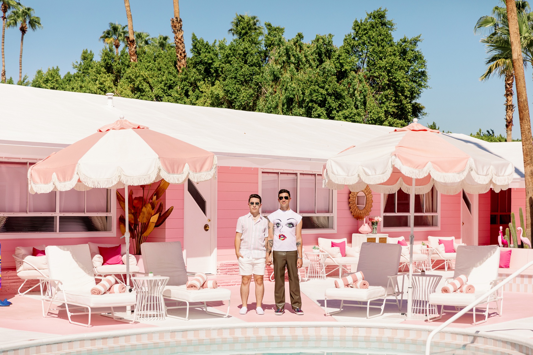 A couple stand holding hands in pink shirts while standing by the pool