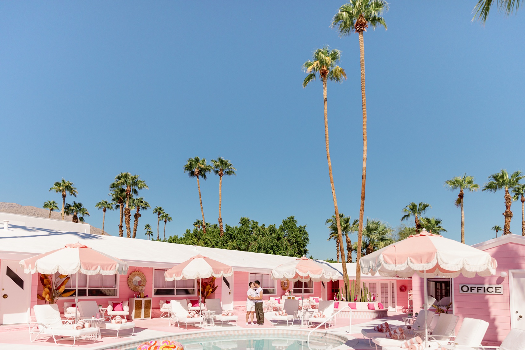 Two groom kiss by the pool under clear blue skies at trixie motel palm springs
