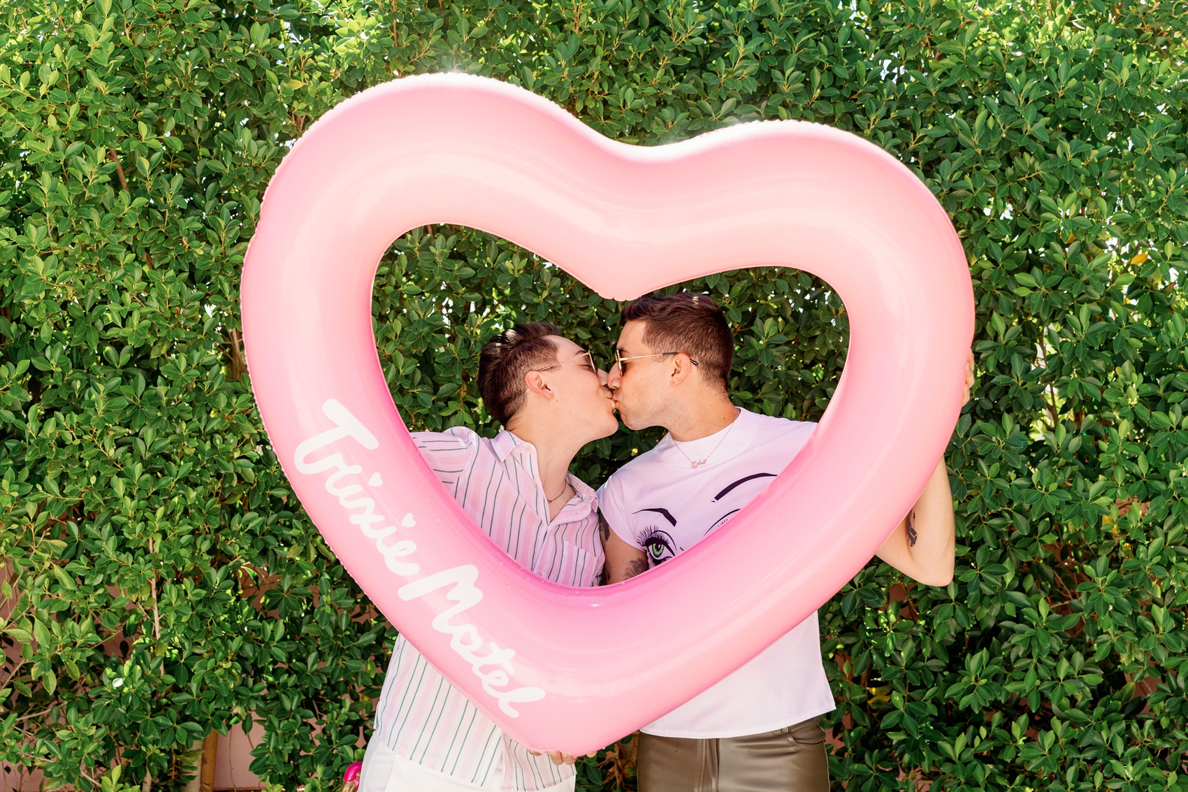 A happy engaged couple kisses behind a heart shaped trixie motel palm springs pool tube