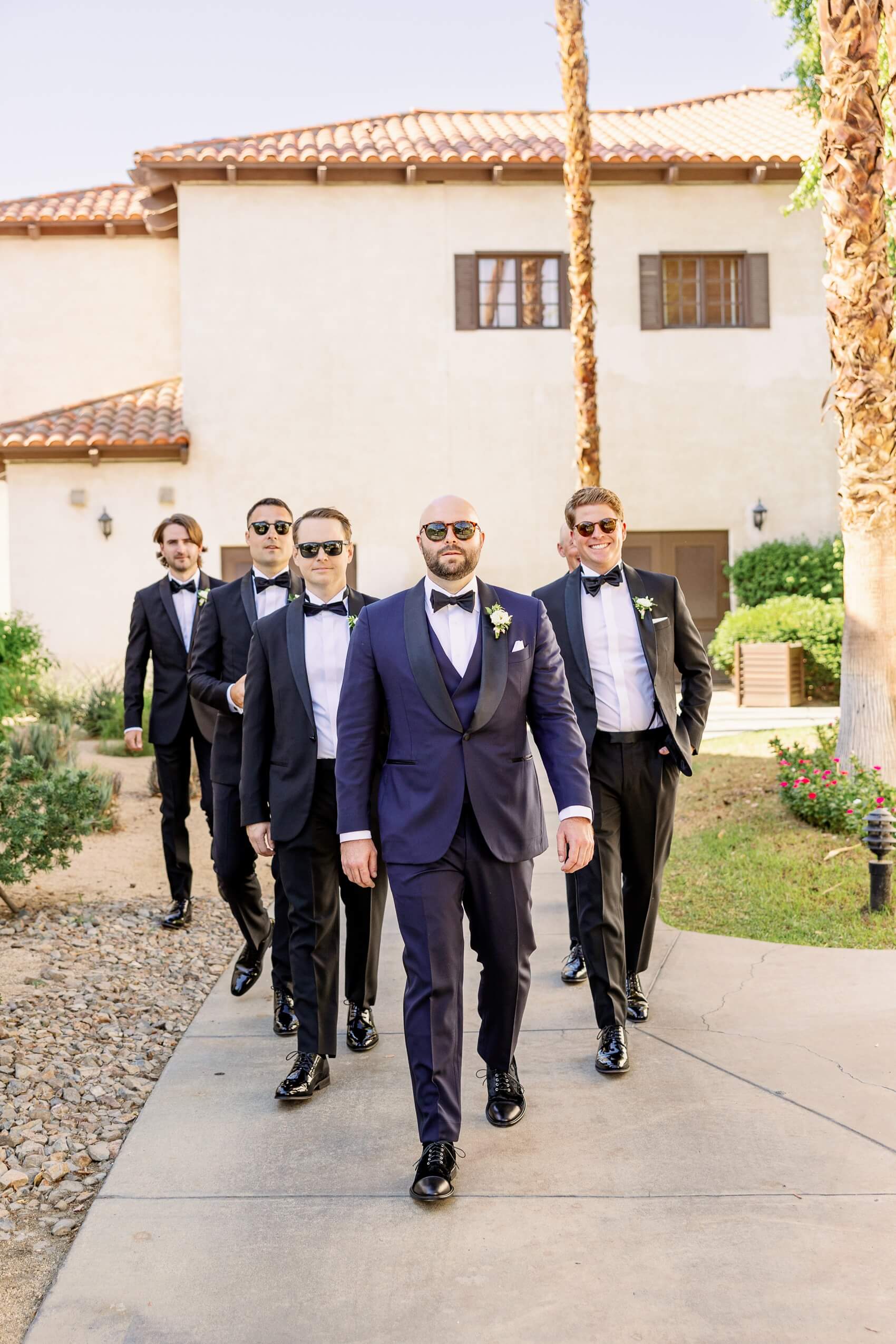 A groom walks a sidewalk with her groomsmen in sunglasses at his rancho las palmas wedding