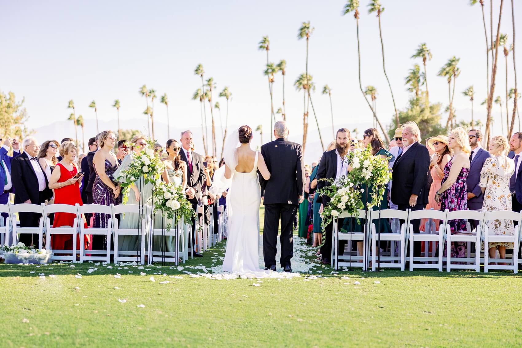 A bride prepares to walk down the aisle with her father as guests turn to see her in the rancho las palmas wedding venue lawn