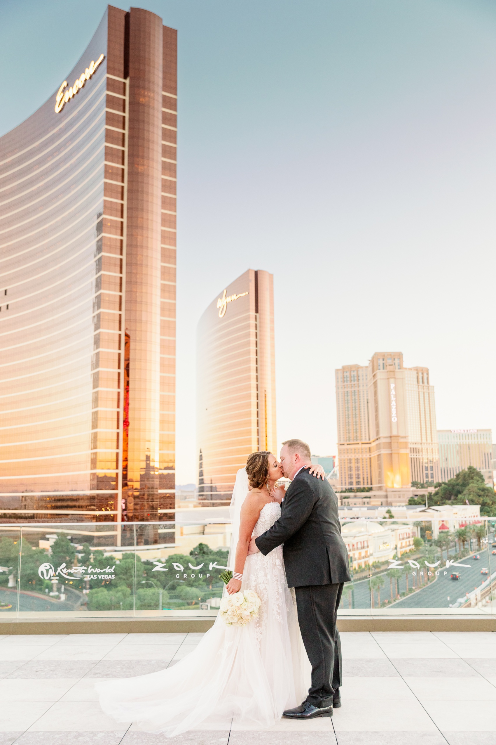 A bride and groom kiss on a rooftop with the encore shining at sunset
