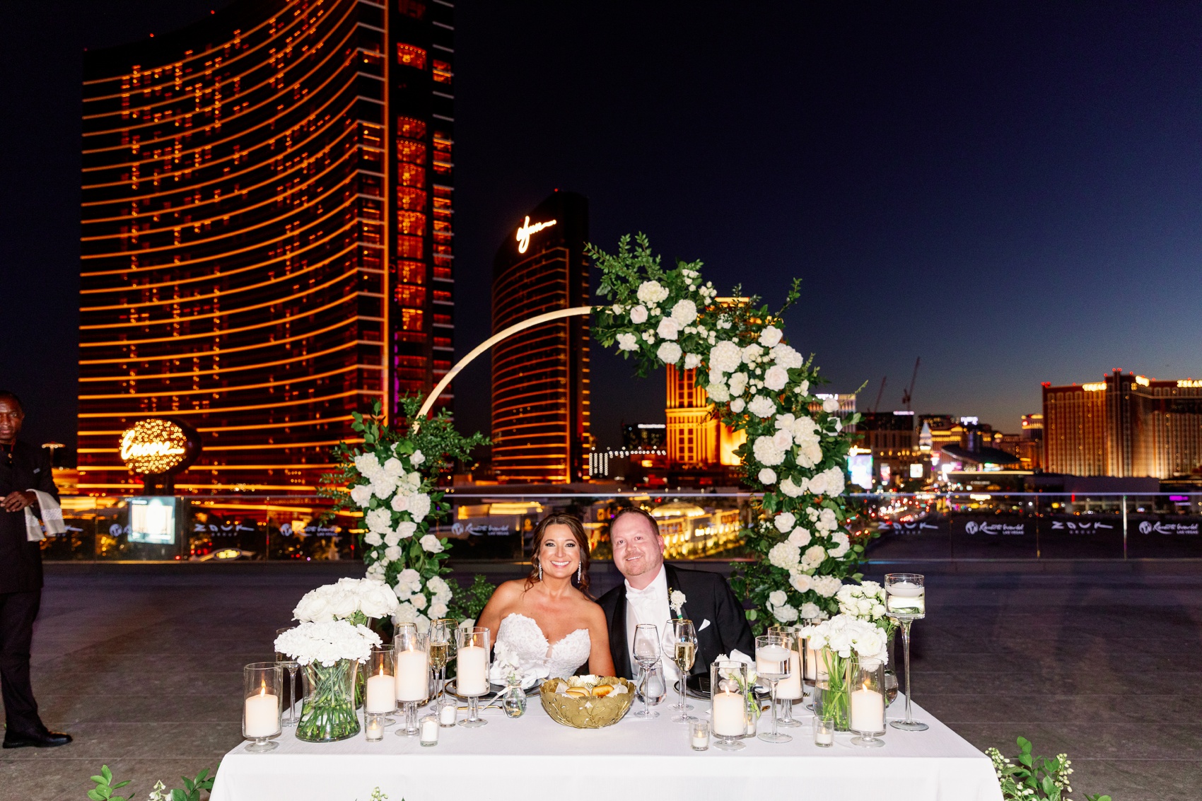 Newlyweds sit at their head able with a flower arch during their rooftop resorts world wedding reception after sunset