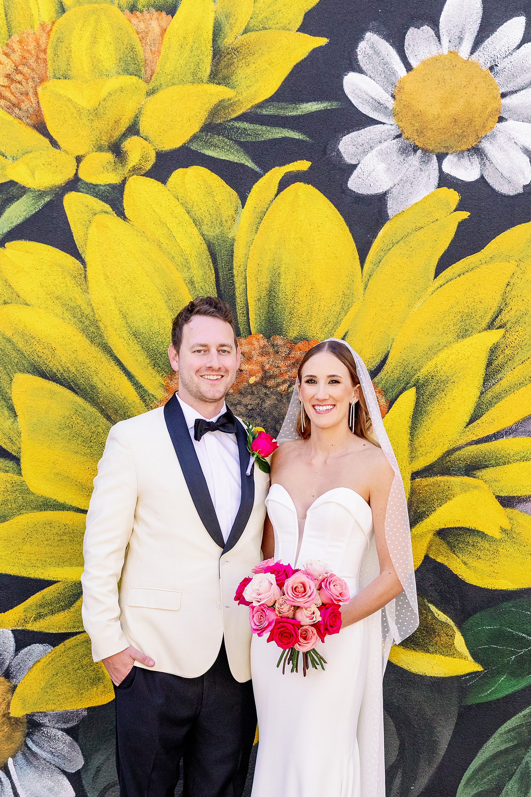 Newlyweds smile against a vibrant flower mural