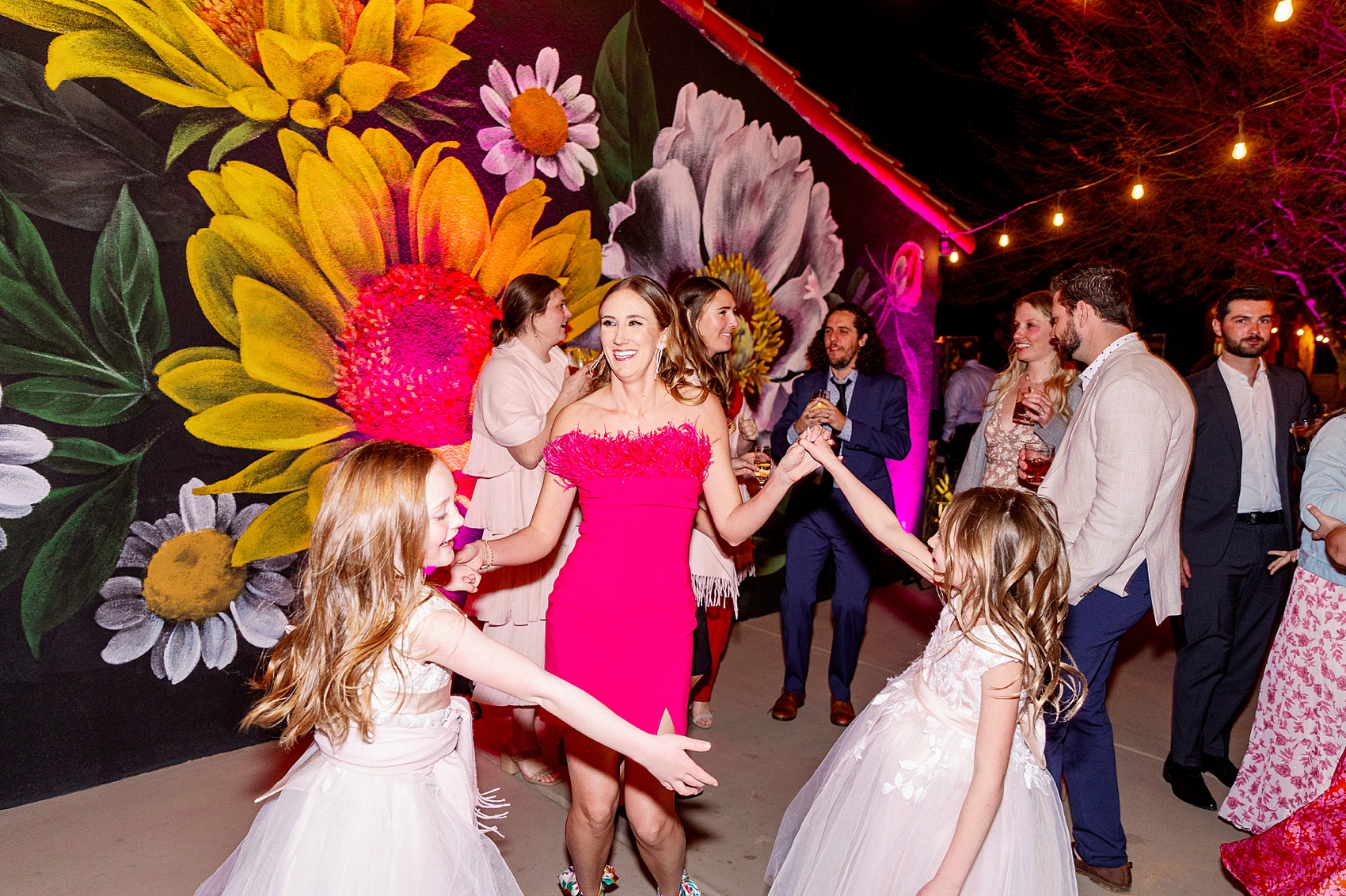 A woman in pink dances with two young girls in gowns at Fleur Noire Hotel wedding