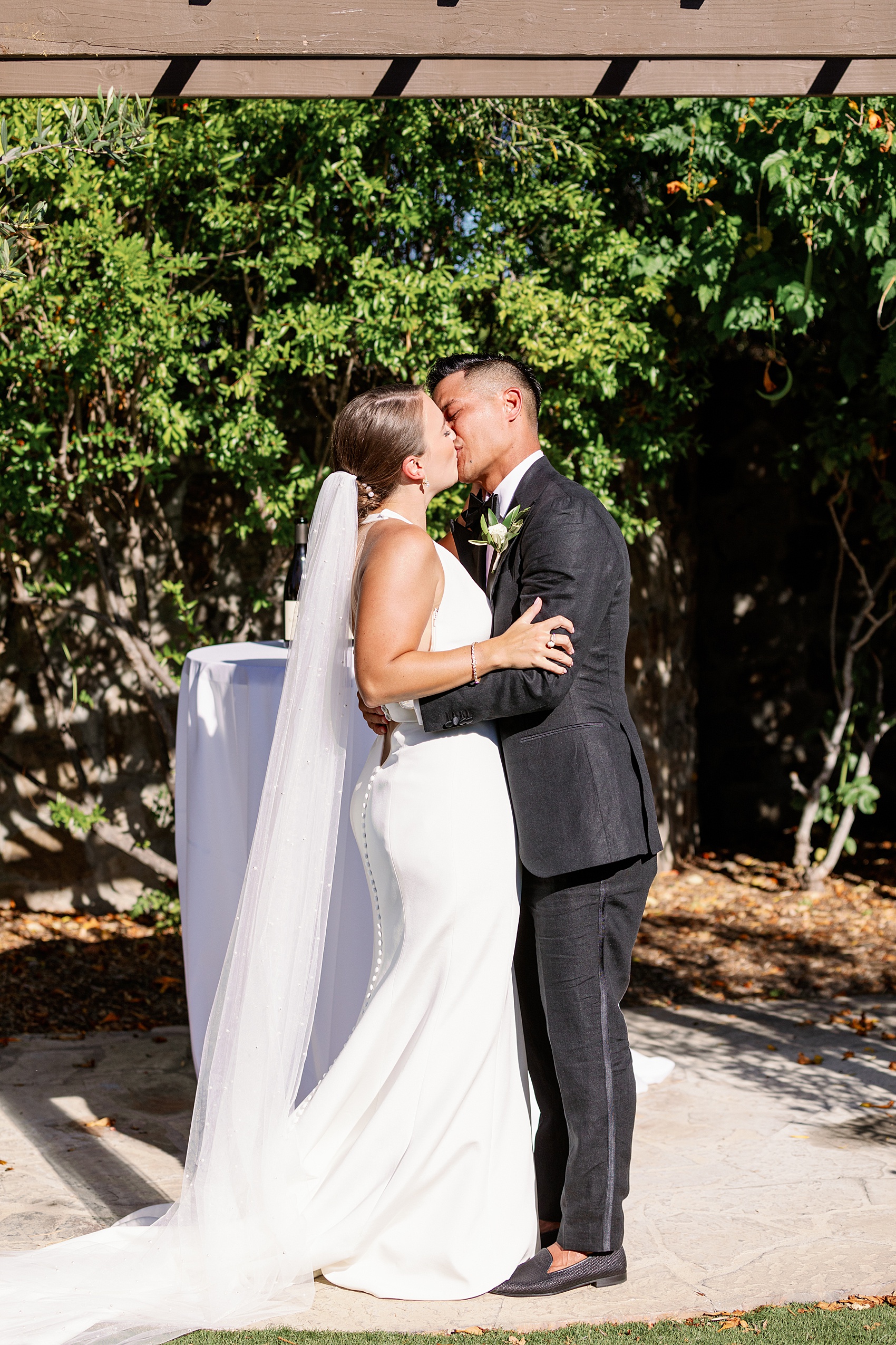 Newlyweds kiss to end their outdoor ceremony under a pergola