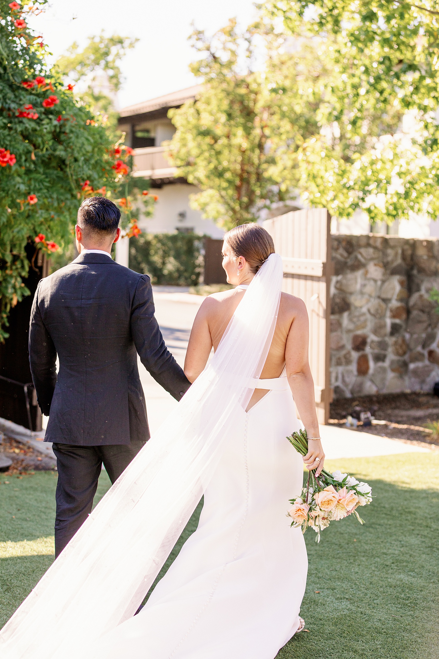 Newlyweds walk holding hands in the gardens at sunset