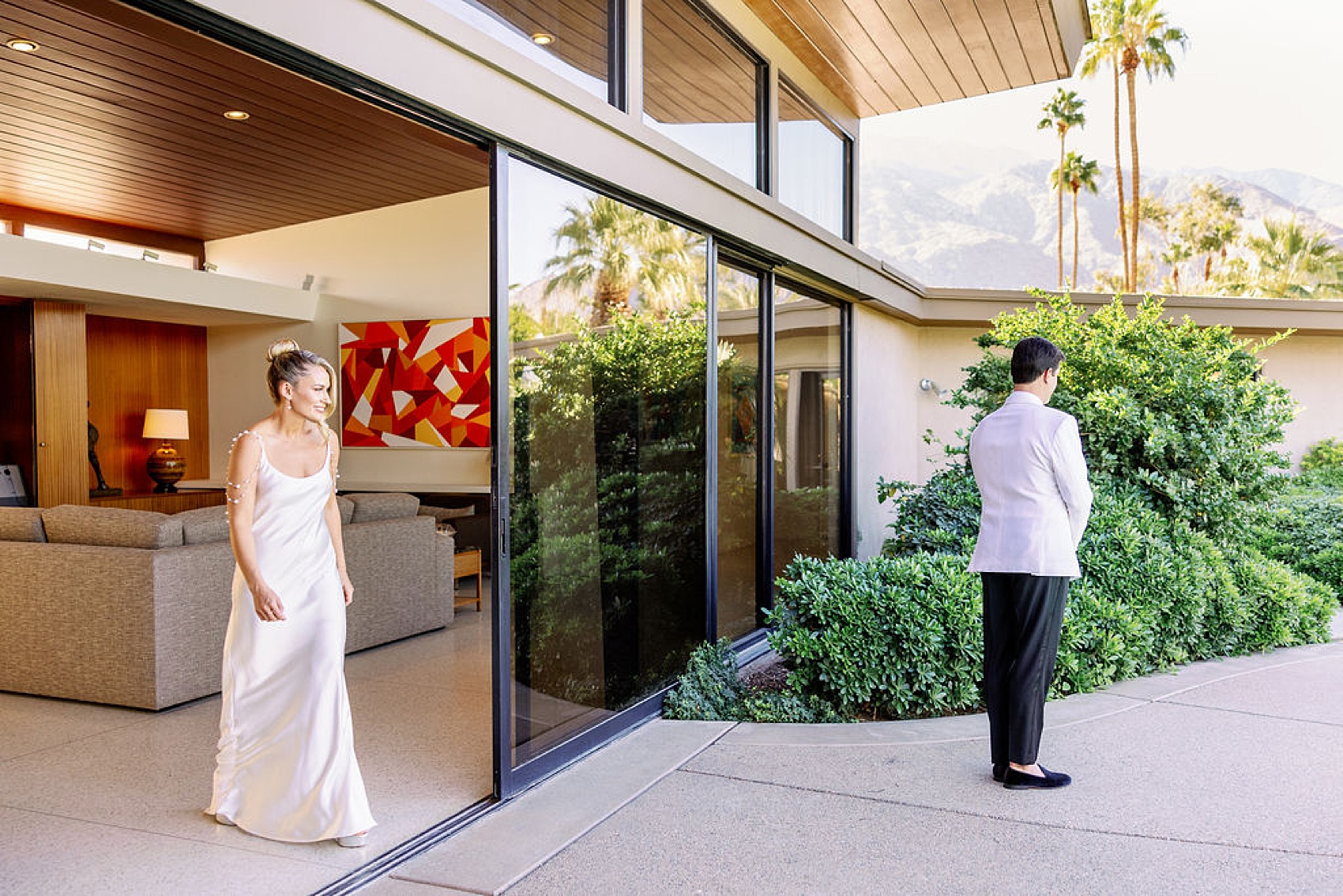 A brie approaches the back of her groom as he awaits their first look on the Frank Sinatra Estate wedding venue patio