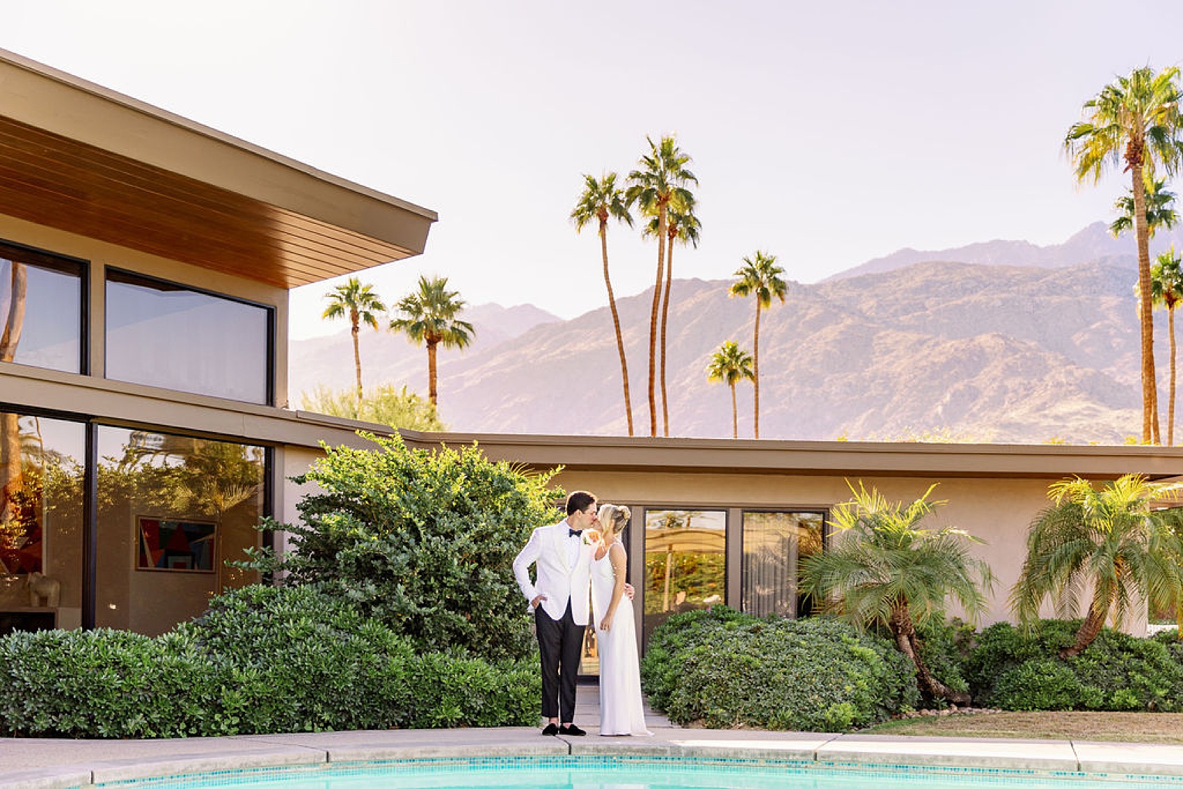 Newlyweds kiss at sunset while standing by the pool of the Frank Sinatra Estate wedding venue