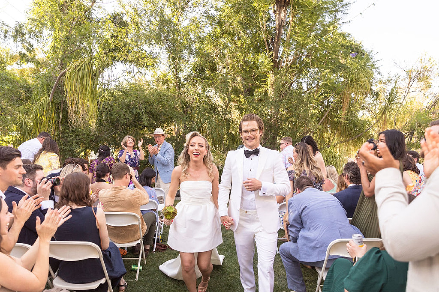 A bride and groom smile while walking up the aisle to applause to end their outdoor palm springs elopement