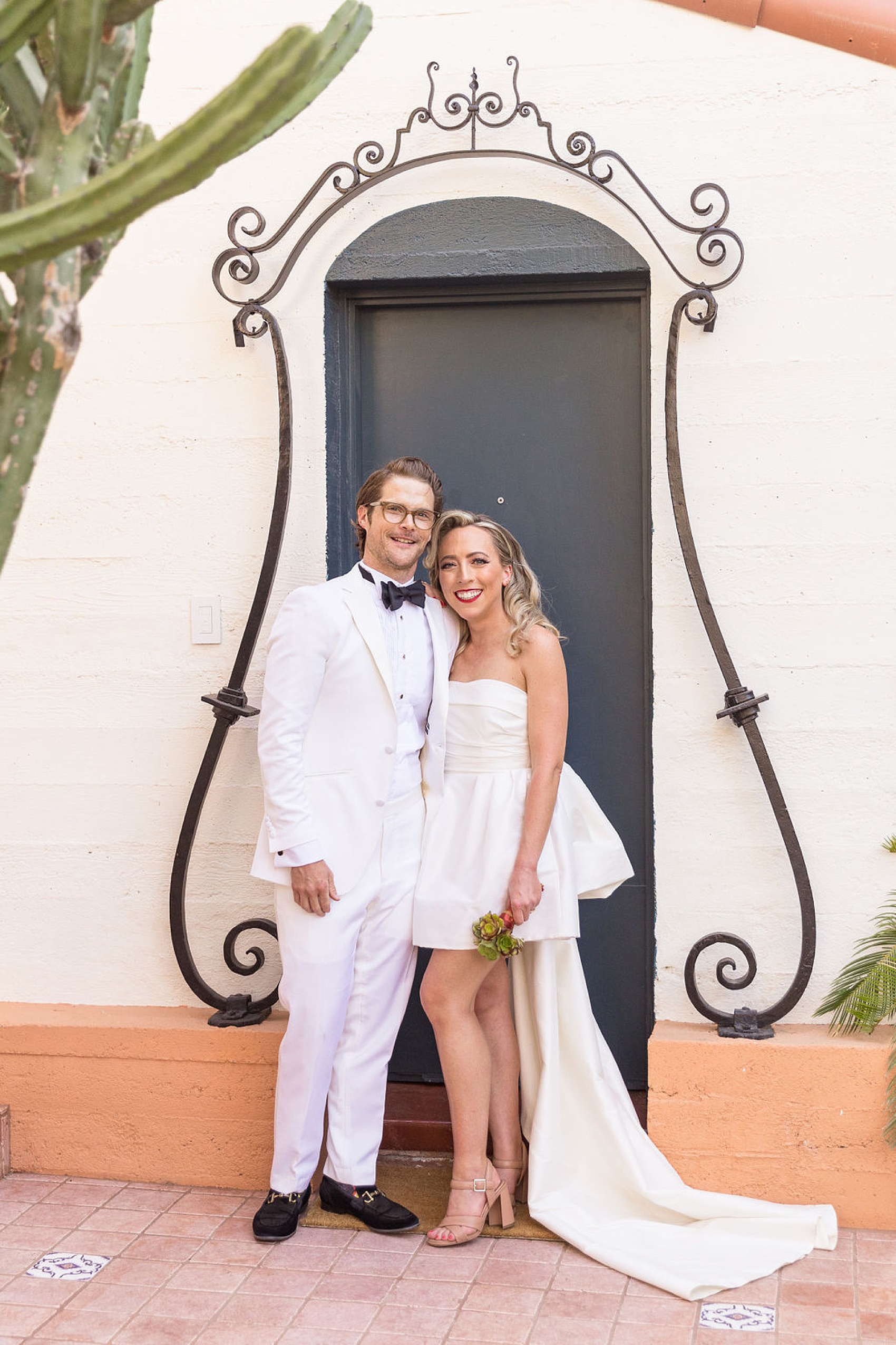 Newlyweds stand smiling together in a doorway with cast iron decorations framing it at their palm springs elopement