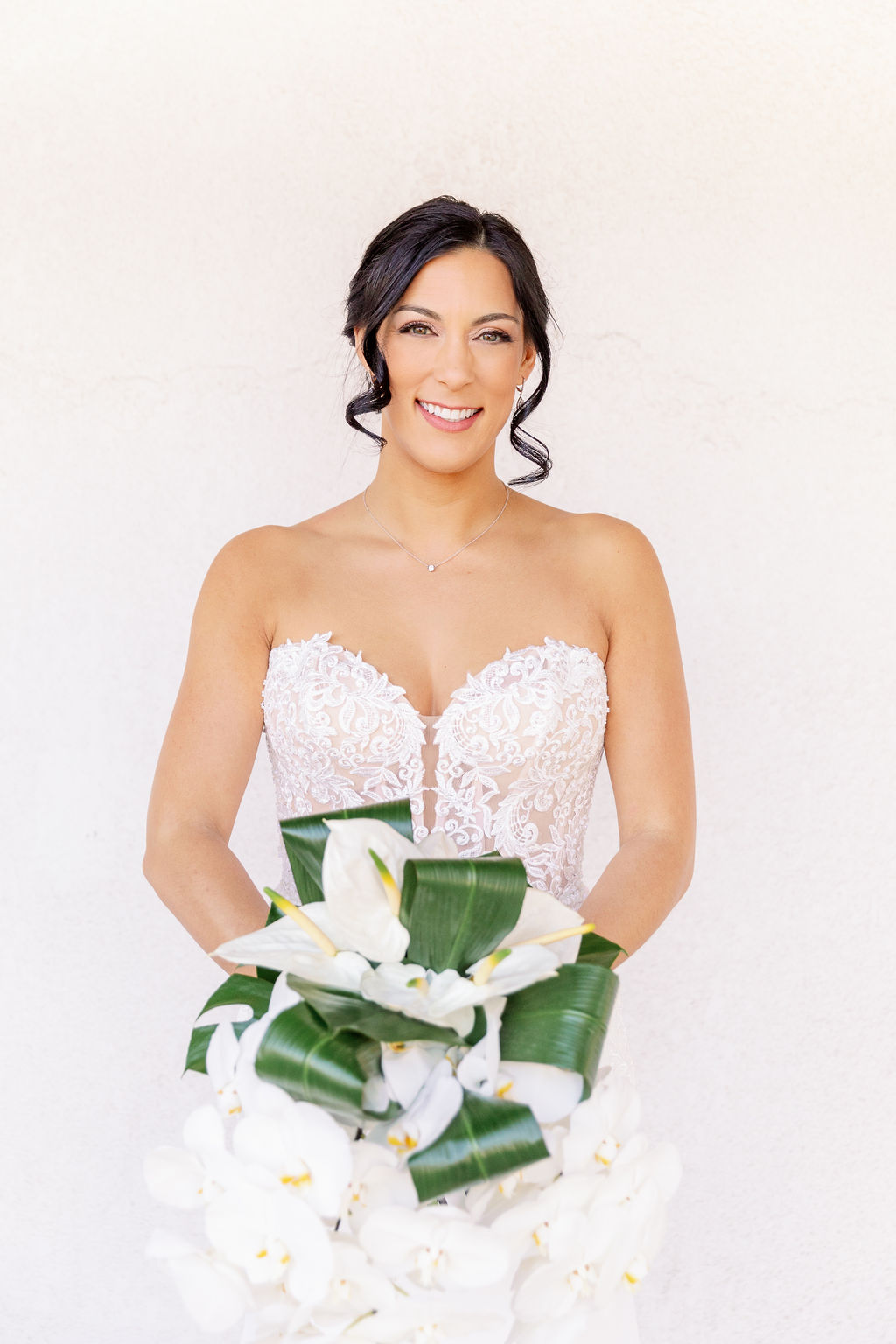 A happy bride in a lace gown holding a large white orchid bouquet