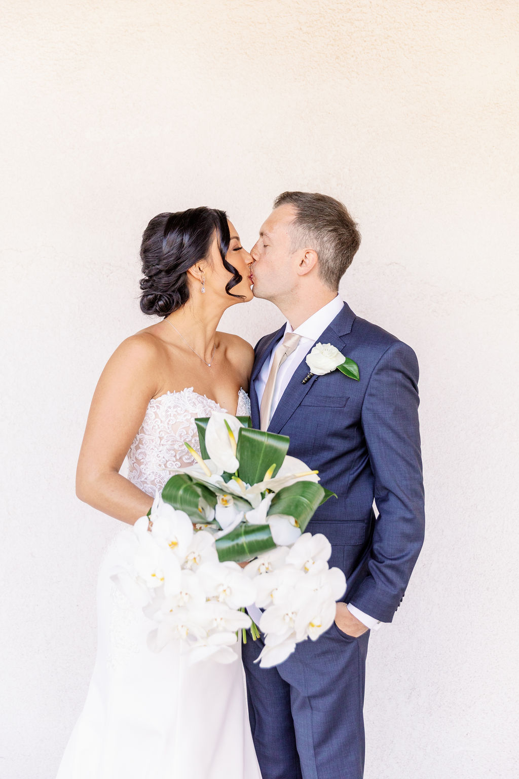 Newlyweds kiss while standing against a white wall