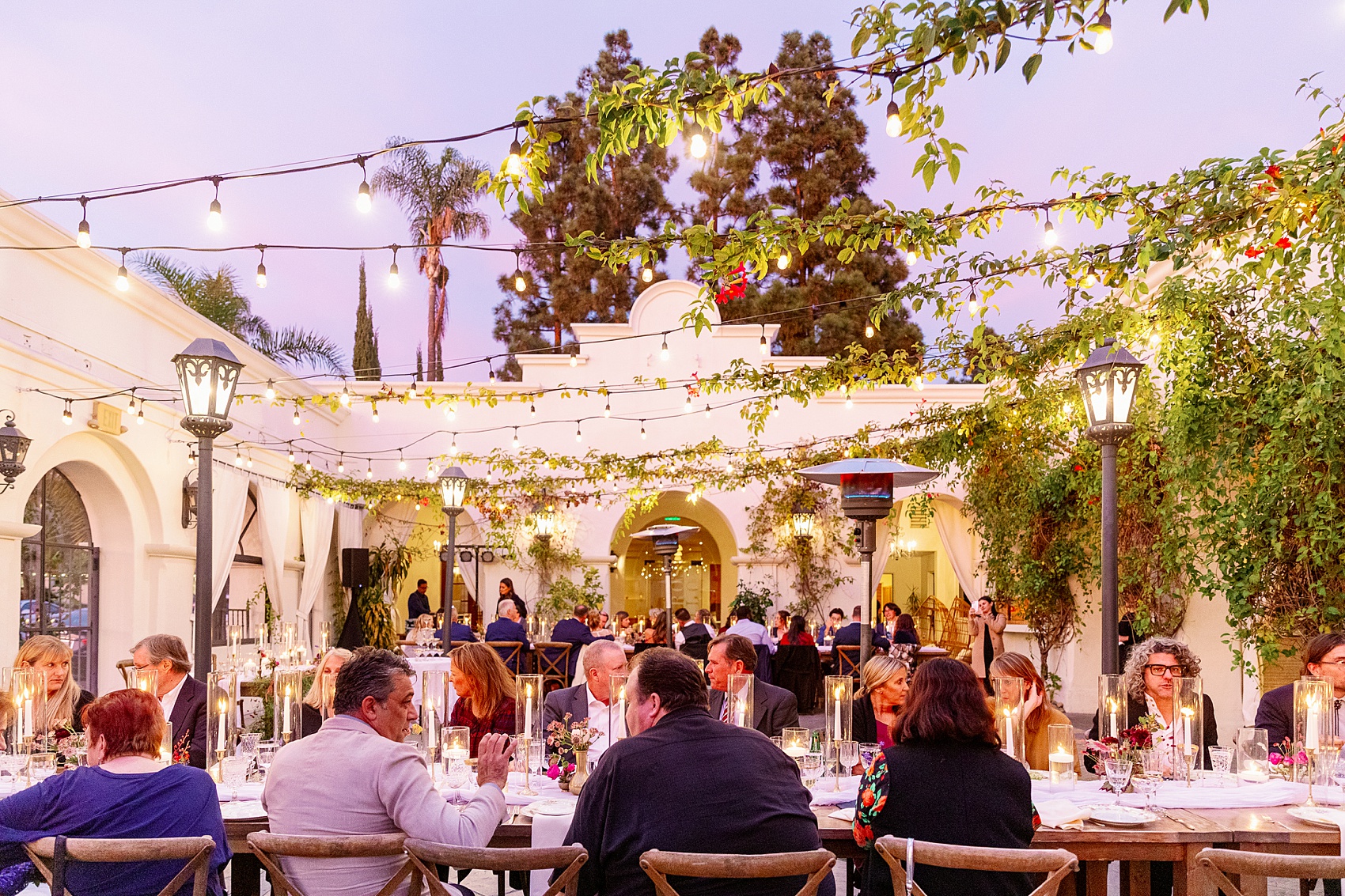 A look at an active wedding reception with everyone seated under market lights at sunset at the villa and vine wedding venue