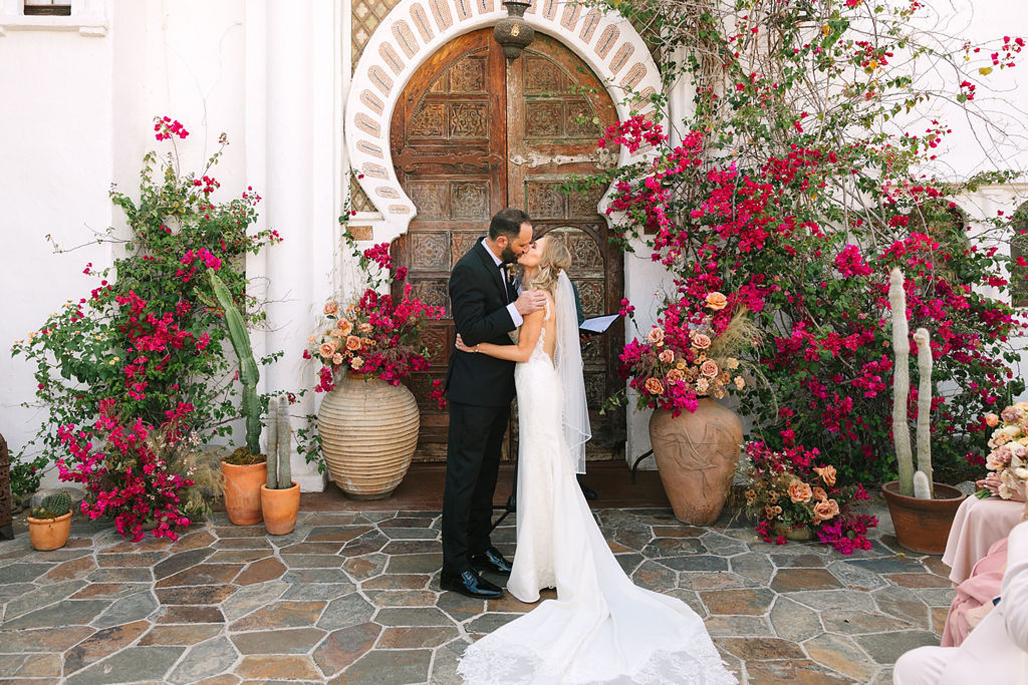 Newlyweds kiss surrounded by pink flowers in a garden patio during their korakia pensione wedding