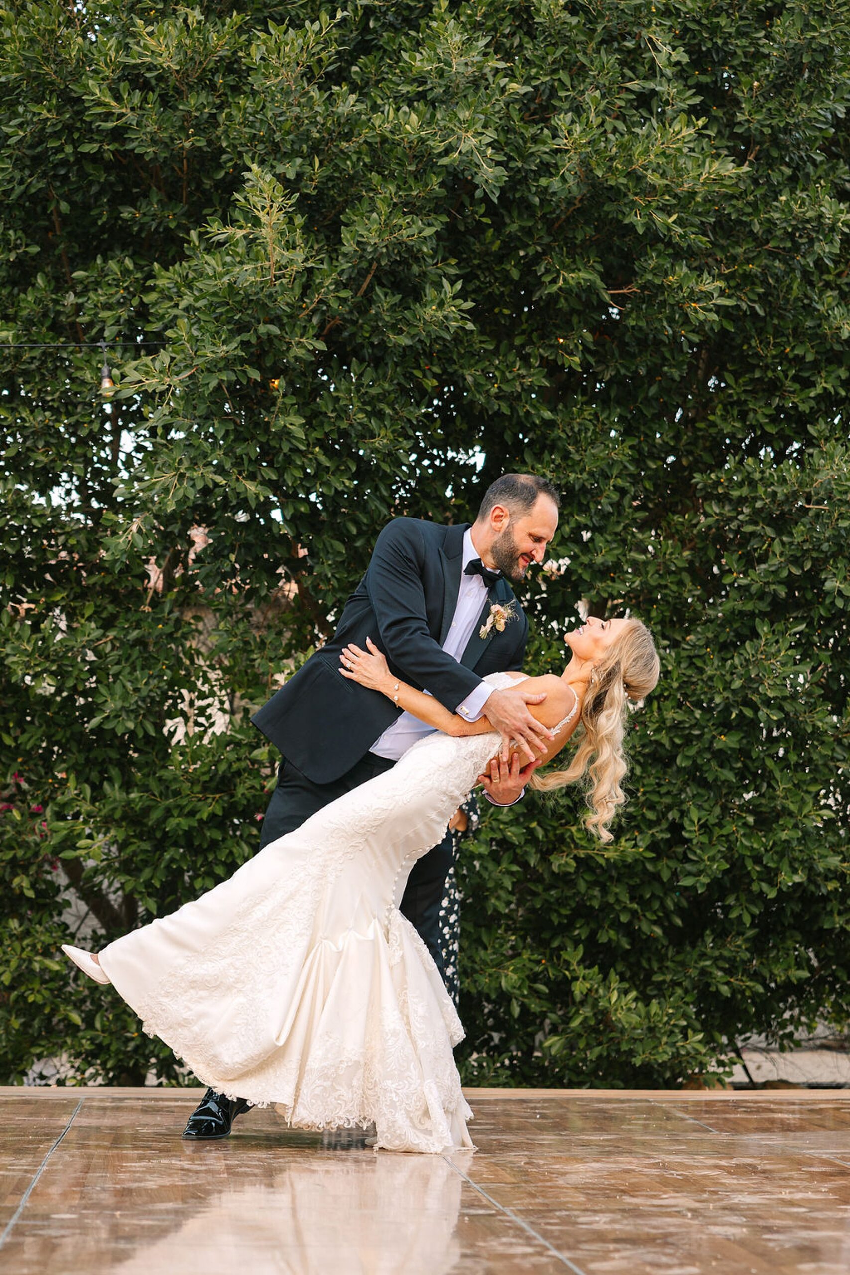 A groom dips his bride while dancing in the garden